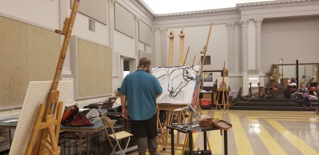 Ryan standing in front of a large canvas, painting his cat, Mabel